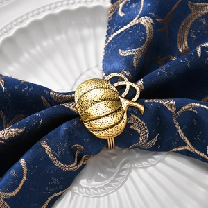Golden pumpkin napkin ring with textured metal on a blue baroque patterned fabric cloth