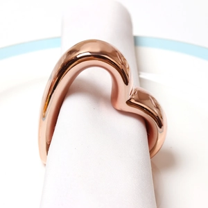 Modern rose gold heart napkin ring set on a white napkin over a premium ceramic plate