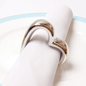 Close-up of polished silver heart napkin ring on white linen set for elegant dining
