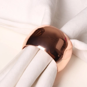 Close-up of polished rose gold rose-shaped napkin ring on a white linen napkin