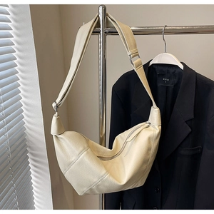 Detail of a cream crescent crossbody bag with lychee texture hanging on a silver hanger