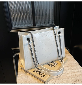 Detailed view of white quilted faux leather tote bag with black metal chain shoulder strap