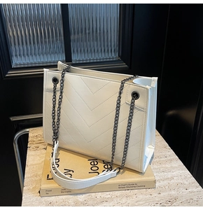 Close-up of white quilted tote bag with V-shaped stitching and chain shoulder strap