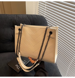 Detail of white quilted tote bag with V-shaped stitching and black metal chain strap