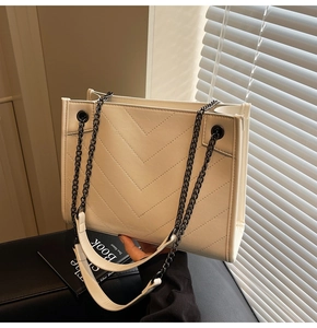 Detailed close-up of white quilted handbag featuring V-shaped stitching and metal chain strap