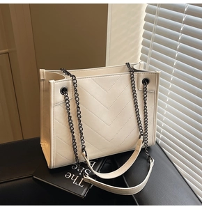 Close-up of cream white tote bag with V-shaped quilting and chain shoulder strap on leather