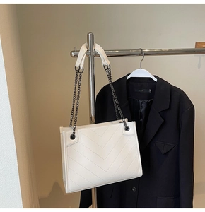 Close-up of white quilted tote bag with V-shaped stitching and dark metal chain strap
