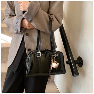 Detail of black glossy leather tote bag with silver hardware and baseball keychain accessory