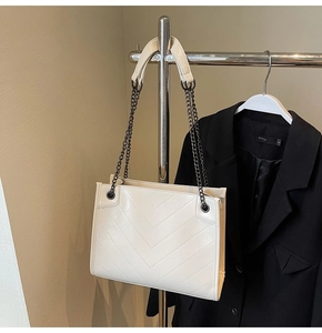 Detail of white tote bag showing V-shaped quilted texture and metal chain strap