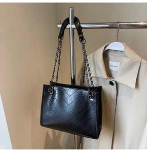 Detail view of the V-shaped chevron quilting and dark metal chain on the black tote bag
