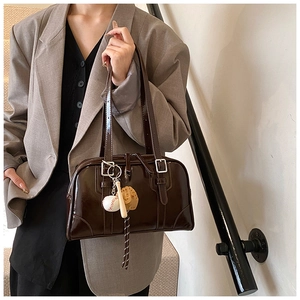 Detail of dark brown patent leather underarm bag with silver buckle and sports charm
