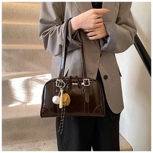 Close-up of dark brown glossy leather tote bag with silver buckle and baseball charms
