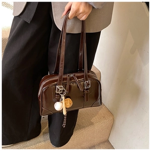 Detail of dark brown patent leather underarm bag with baseball theme charms