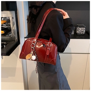 Detail of burgundy glossy leather underarm bag with silver buckles and baseball charm