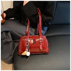 Detail of a dark red Boston bag with shiny finish and a baseball glove charm