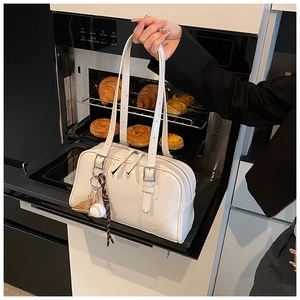 Detail of cream faux leather tote with sports charms held against an oven background