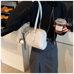 Detail of white leather shoulder bag with silver zipper and baseball charm accessory