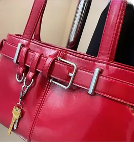 Close-up of bright red patent leather handbag featuring silver buckles and key charms