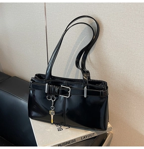 Detail of black patent leather shoulder bag with belt buckles and gold key pendant charm