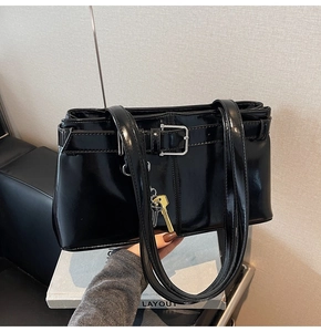 Detail of glossy black shoulder bag featuring dual key charms and buckle straps decoration