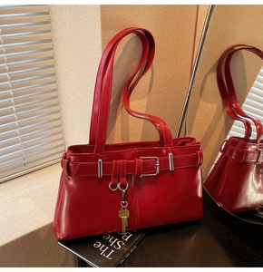 Detail of red glossy shoulder bag with silver buckles and gold key charm on books