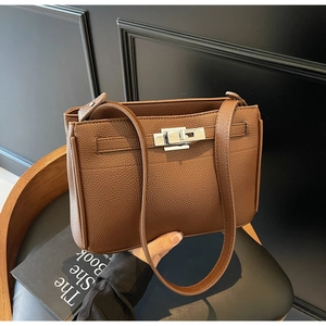 Detail of brown litchi leather handbag with silver lock on a black leather chair
