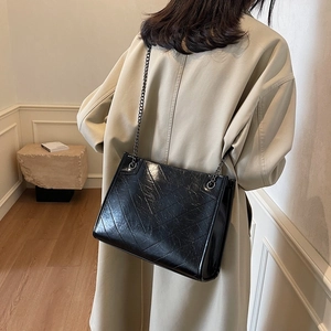 Chic black chain shoulder bag in pleated leather worn with a beige coat for a stylish look