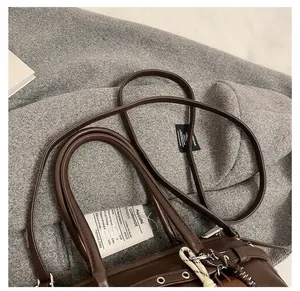 Detail of dark brown leather handbag featuring dual handles and metallic eyelet accents