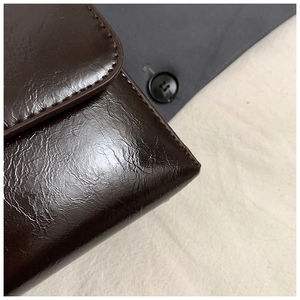 Close-up of dark brown glossy leather handbag showing fine stitching and retro texture