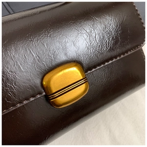 Detail of dark brown leather square bag featuring a vintage gold oval metal clasp closure