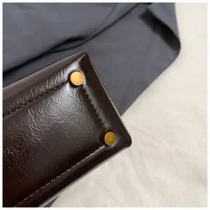 Detail view of dark brown leather handbag base with gold studs and precise stitching