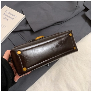 Detailed base view of dark brown leather handbag with protective gold metal feet studs
