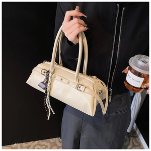Detail of beige leather baguette bag with metal eyelets and decorative tassel charm