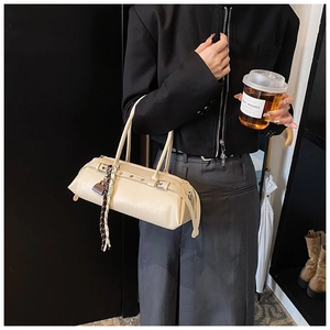 Detail of cream baguette bag with buckle strap and decorative scarf on a shoulder