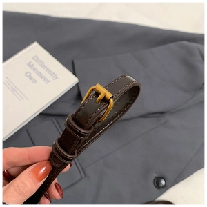 Close-up of a dark brown glossy leather belt featuring a classic gold pin buckle detail
