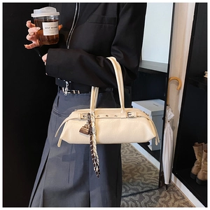 Detail of cream rectangular underarm bag with decorative metal eyelets and a silk scarf charm