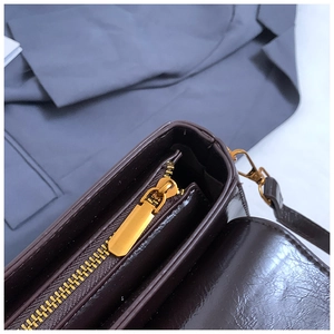 Detail of glossy brown leather bag showing premium gold metal zipper and smooth texture