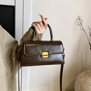Detail of dark brown glossy leather handbag featuring golden clasp and retro texture