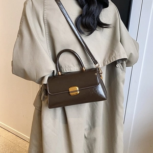 Dark brown glossy crossbody bag with gold lock styled on a beige trench coat for autumn