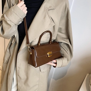 Detail of a dark brown glossy leather handbag with gold twist lock on a beige trench coat
