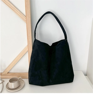 Close-up of minimalist black matte suede tote bag with wide strap on a clean desktop