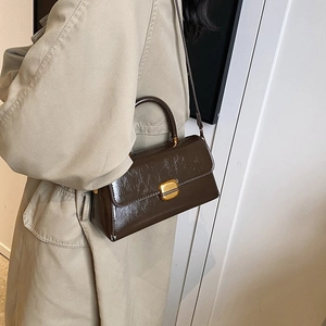 Close-up of vintage brown leather handbag with gold metal clasp on a beige trench coat