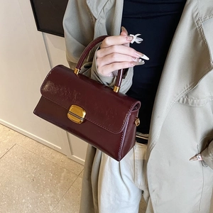 Close-up of a burgundy leather handbag with a gold square buckle and round handle