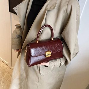 Close-up of burgundy oil-wax leather handbag with gold clasp and top handle for women