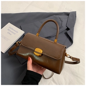 Detail of dark brown leather square handbag with golden rotating buckle and round handle