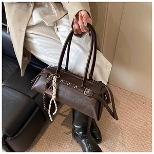 Detail of dark brown leather baguette bag with silver grommets and woven knot accessory