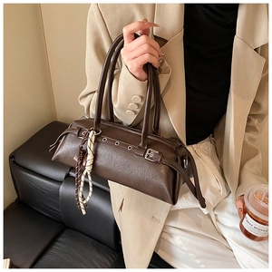Detail of dark brown baguette bag with metal rings and woven knot charm on a beige suit