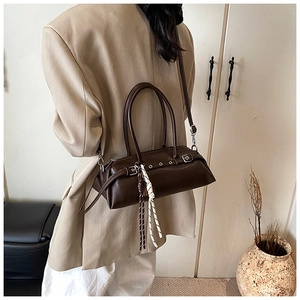 Detail of dark brown leather baguette bag with silver hardware and woven tassel