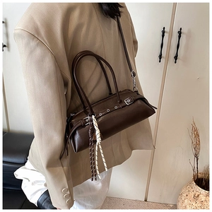 Detail of dark brown leather baguette bag with metal eyelets and rope charm on a model