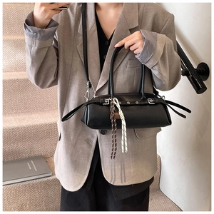 Detail of black cylindrical pillow bag with metallic eyelets and woven tassel charm